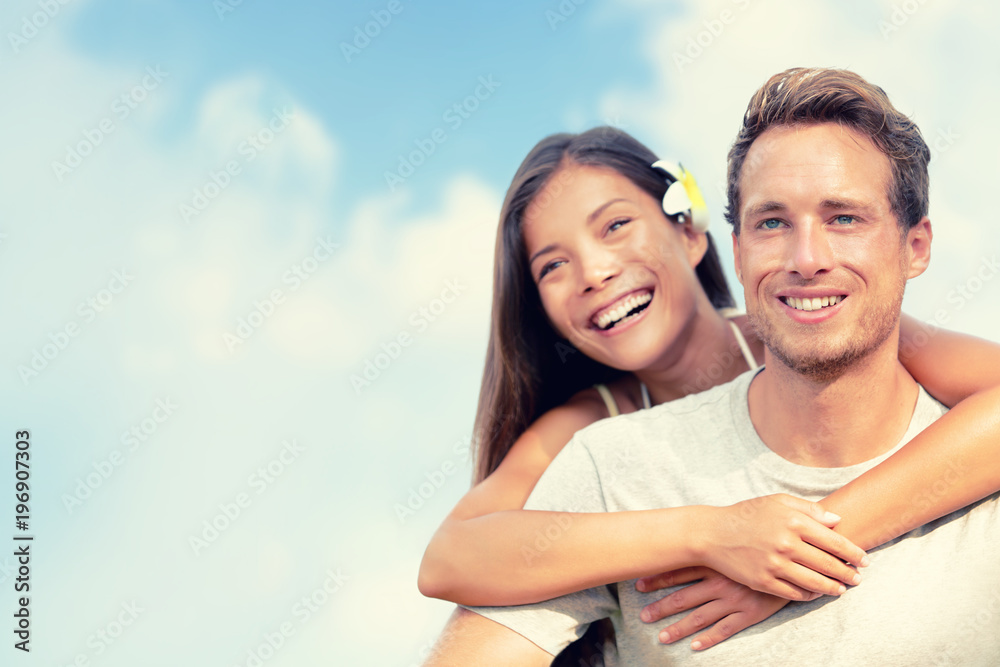 Happy couple hugging in summer blue sky background. Smiling young people tourists on travel vacation. Asian girl piggyback on man. Healthy lifestyle. Happy couple hugging in summer blue sky background. Smiling young people tourists on travel vacation. Asian girl piggyback on man. Healthy lifestyle.