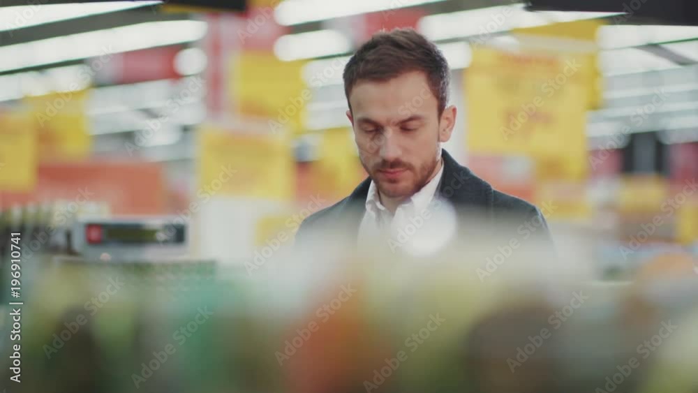 young man walking in supermarket with shopping trolley which looking on shopping list in phone light choose fruit buyer customer business food face store adult market male retail slow motion young man walking in supermarket with shopping trolley which looking on shopping list in phone light choose fruit buyer customer business food face store adult market male retail slow motion