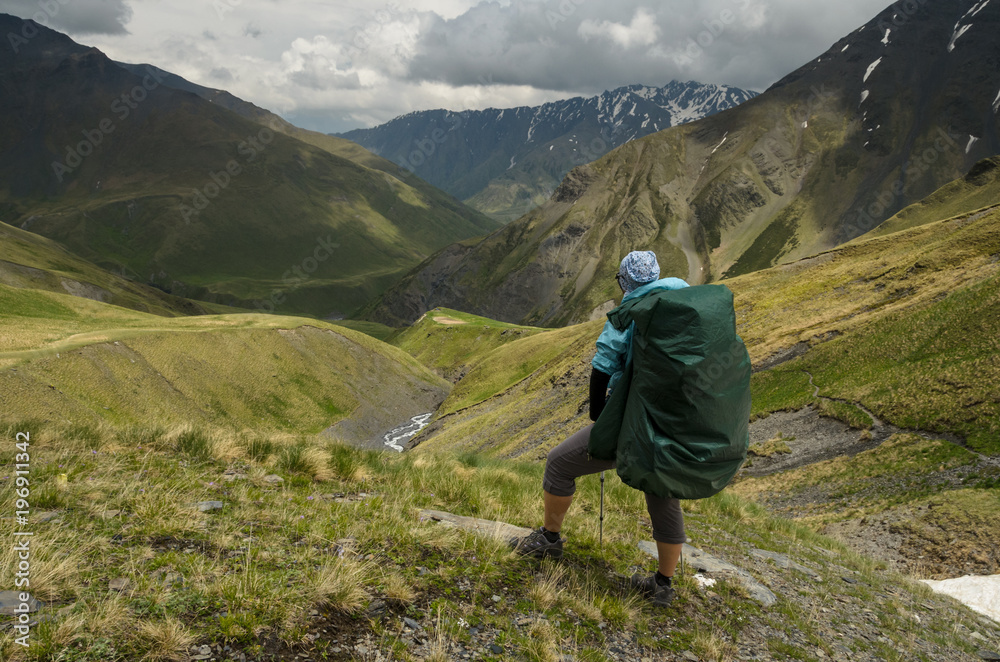 Backpacker girl on the mountain trail looks down to the valley. Epic view to Caucasus mountains at Tusheti (Georgia). Concept of travel lifestyle photo. 
