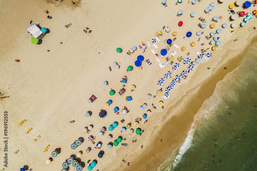 Aerial top view of people relaxing on the beach with ocean and colorful umbrellas