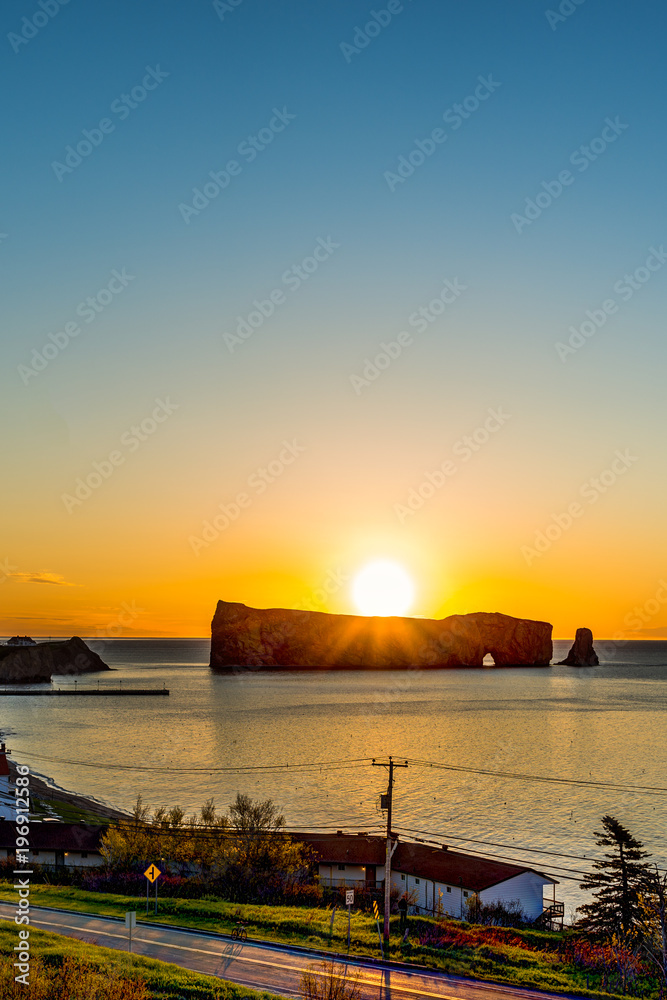 Famous Rocher Perce rock in Gaspe Peninsula, Quebec, Canada, Gaspesie region with cityscape at sunrise and sun, small town
