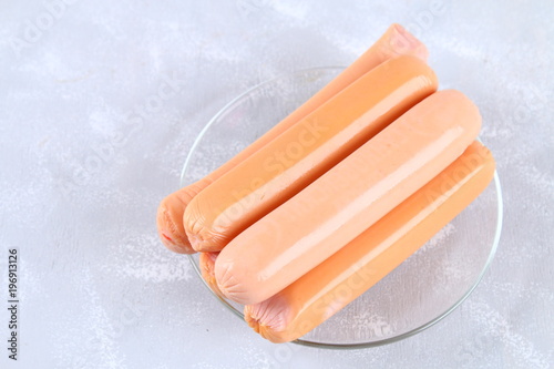 Raw sausages on a wooden board on a gray concrete table.