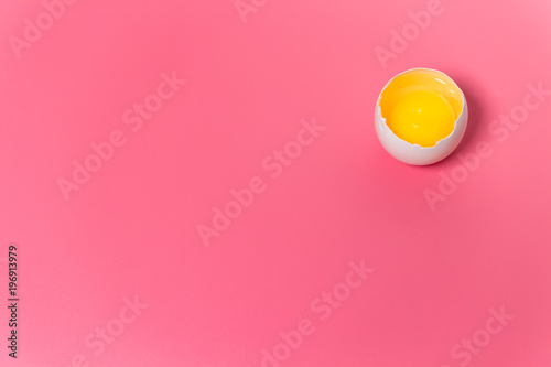 Fresh farm chicken egg, food background. Cracked egg with white and yolk over pink. Spring easter theme. Close up. Copy space.