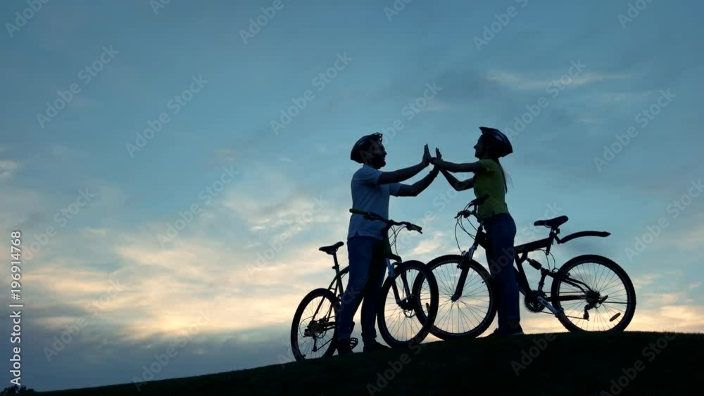 Couple of cyclists clapping hands together. Young man and woman having fun on bicycles at sunset. Best romantic rest together. Couple of cyclists clapping hands together. Young man and woman having fun on bicycles at sunset. Best romantic rest together.