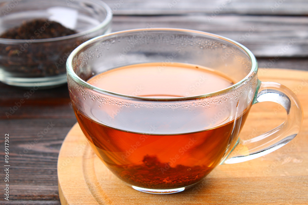 Hot black tea in a glass cup and dry tea on a wooden table. Hot black tea in a glass cup and dry tea on a wooden table.