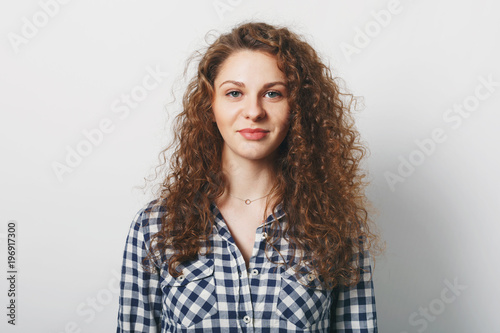Waist up portrait of gorgeous female has curly hairstyle dressed casually, isolated over white background. Pretty woman has healthy skin and attractive look satisfied with something. Facial expression