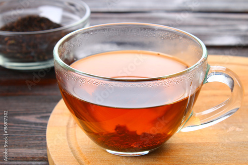 Hot black tea in a glass cup and dry tea on a wooden table.