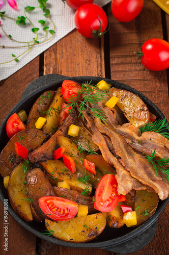 Fried potatoes with bacon and fresh tomatoes in the frying pan. Wooden rustic background. Top view photo