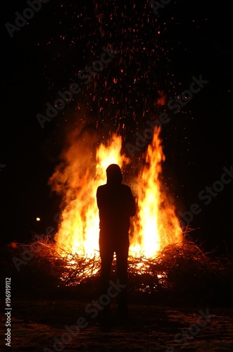 Silhouette of man by the fire at night. Man standing in front of bonfire. Flame on the ground.