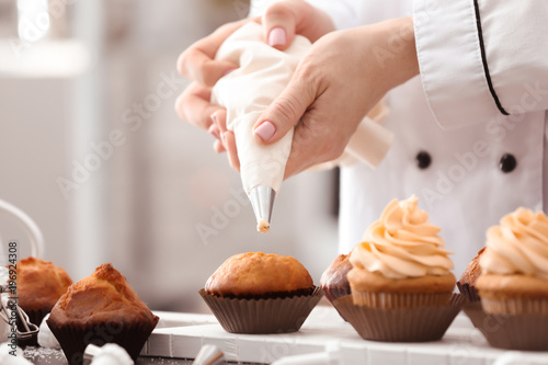 Chef decorating tasty cupcakes with cream at table