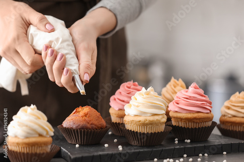 Woman decorating tasty cupcakes with cream at table