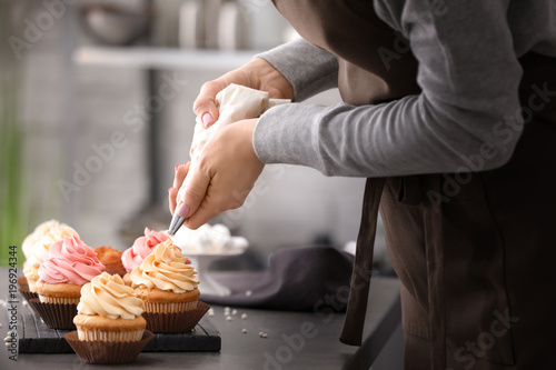 Foto Woman decorating tasty cupcakes with cream at table