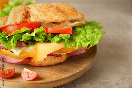 Wooden plate with tasty croissant sandwich, closeup