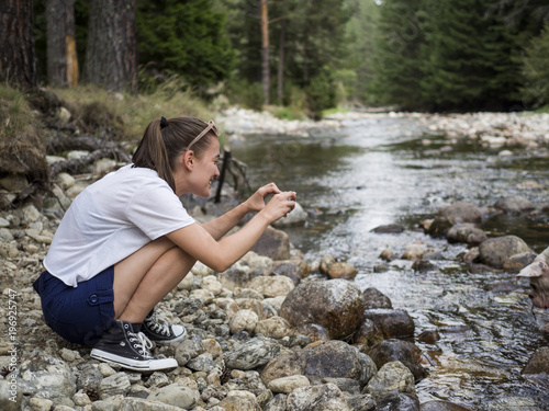 Young female traveler taking pictures of her dog playing in a river