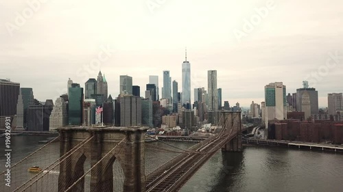 Brooklyn Bridge aerial with American flag moving forward toward Manhattan skyline with Freedom Tower in New York City NYC in 4K and 1080 HD