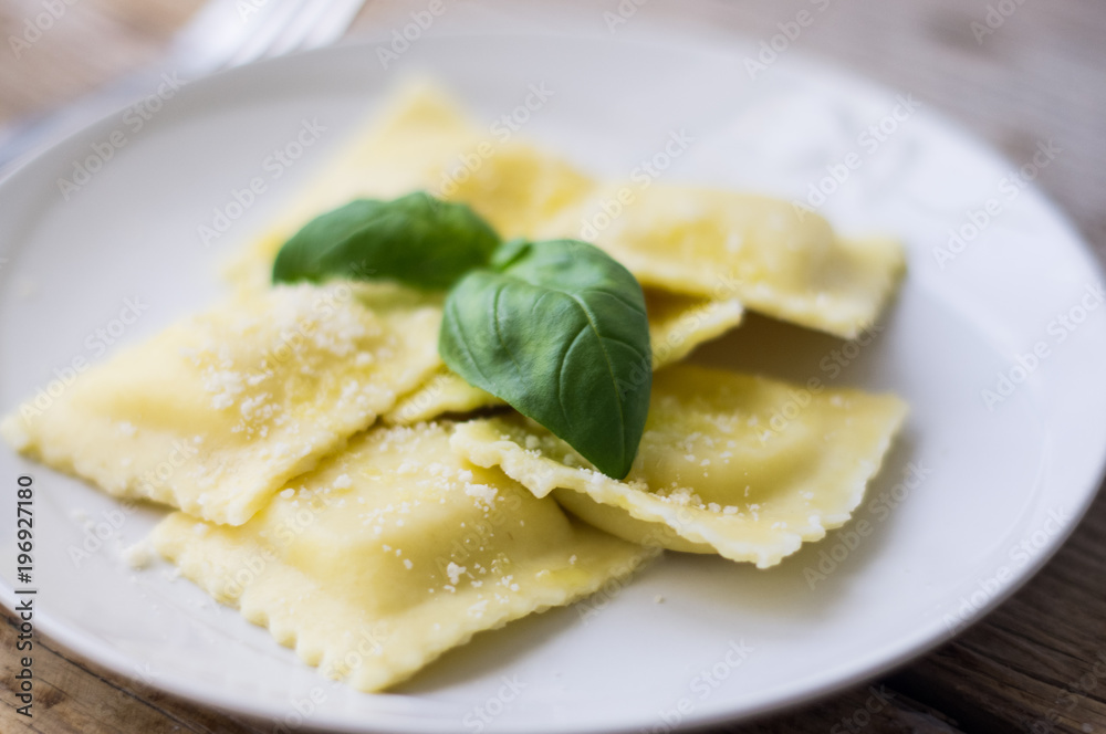 Plate of ravioli with ricotta cheese, basil and grated parmesan cheese on top on wooden table Plate of ravioli with ricotta cheese, basil and grated parmesan cheese on top on wooden table