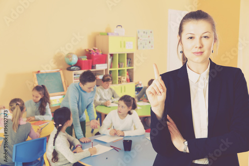 Strict female teacher standing foreground in classroom