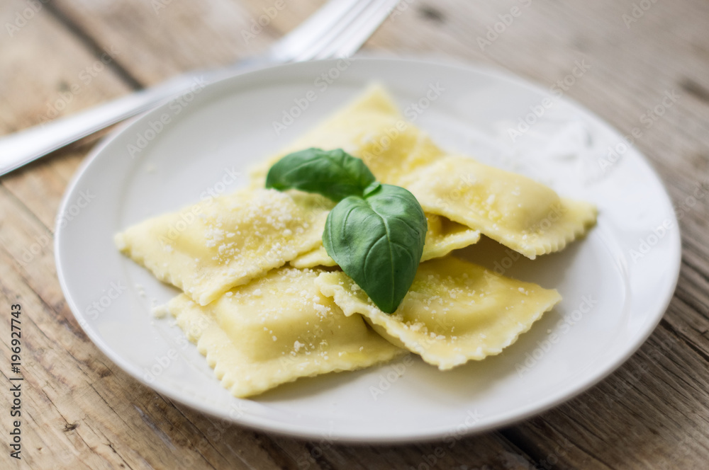 Plate of ravioli with ricotta cheese, basil and grated parmesan cheese on top on wooden table Plate of ravioli with ricotta cheese, basil and grated parmesan cheese on top on wooden table