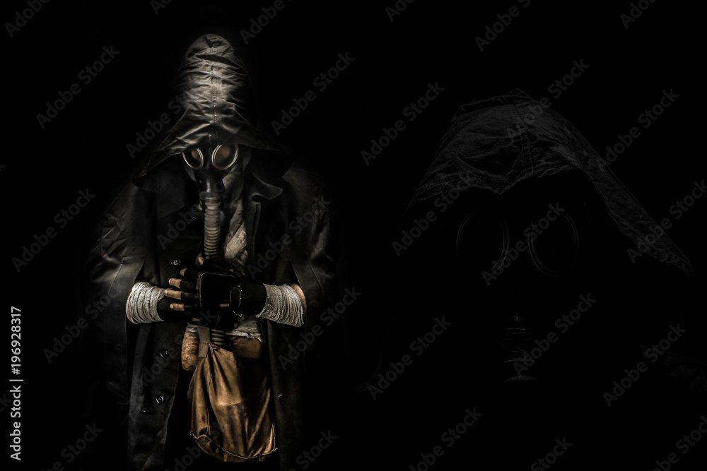 man in the gas mask in the hood, on the black background surrounded by smoke, with hands on the chest, survival soldier after apocalypse.