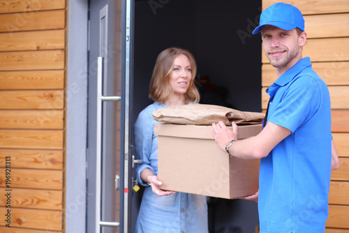 Smiling delivery man in blue uniform delivering parcel box to recipient - courier service concept © lenets_tan