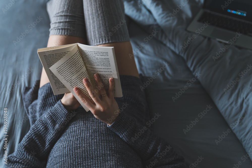 Fototapeta premium woman read book in bed. laptop on background.