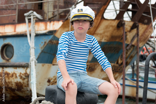 Portrait of a boy in a vest (Telnyashka) and captain's cap against the background of a rusty and old ship.