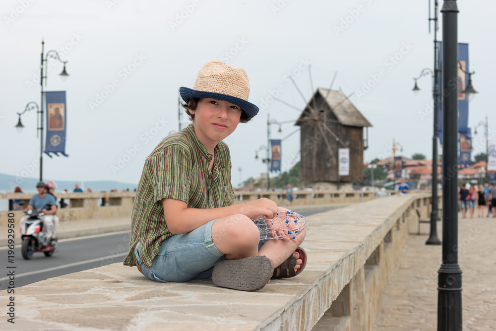 Portrait of a beautiful boy in a short shirt and hat on a blurred background of a wooden windmill and the road.