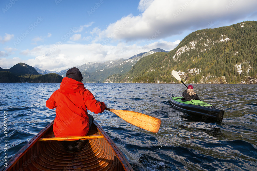 Man canoeing and woman kayaking during a windy winter day. Taken in Indian Arm, Deep Cove, Vancouver, BC, Canada. Concept: adventure, holiday, vacation