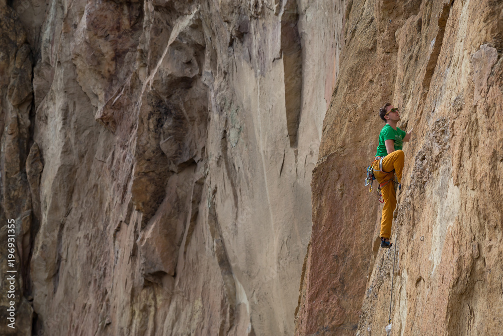 Adventurous man is rock climbing on the side of a steep cliff during a cloudy winter evening. Taken in Smith Rock, Oregon, North America. Adventurous man is rock climbing on the side of a steep cliff during a cloudy winter evening. Taken in Smith Rock, Oregon, North America.