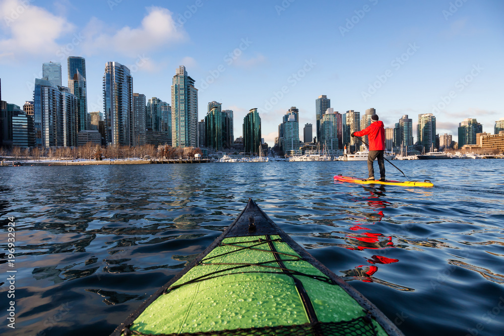 Fototapeta premium Pływanie kajakiem i wiosłem na pokład w Coal Harbour podczas tętniącego życiem, słonecznego poranka. Zrobiono w Downtown Vancouver, British Columbia, Kanada.