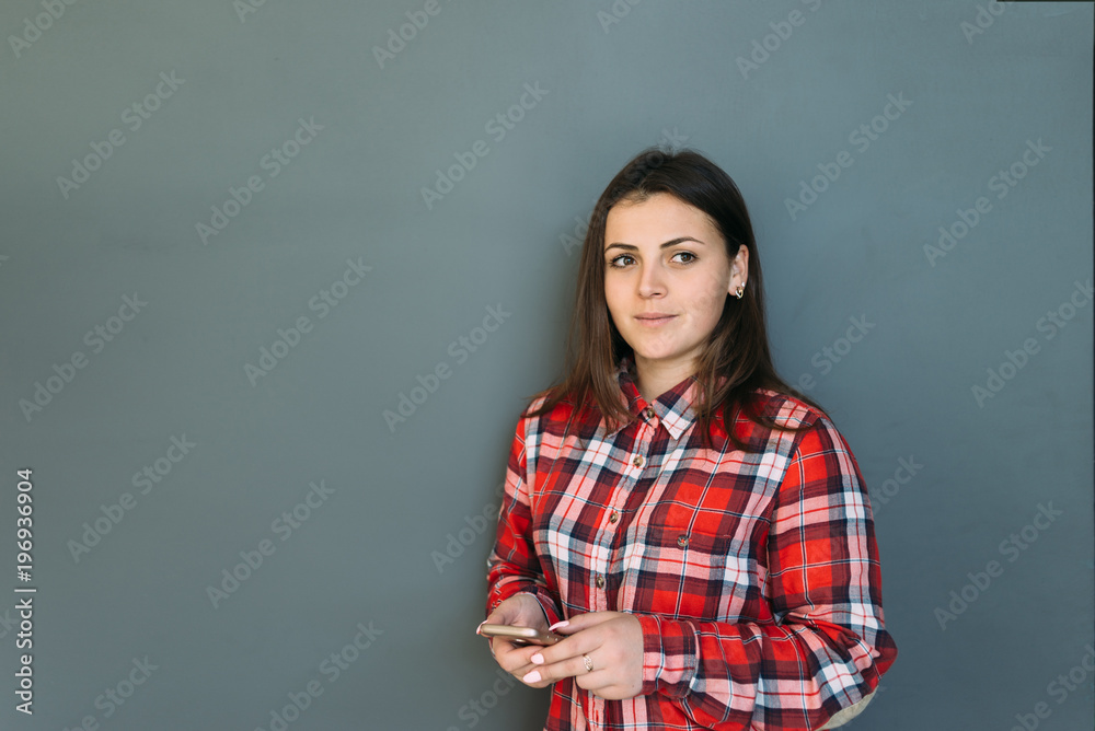 the student is standing by the wall of gray color with the phone in hands the student is standing by the wall of gray color with the phone in hands