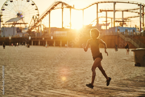 athletic african american woman jogging on boardwalk at sunset