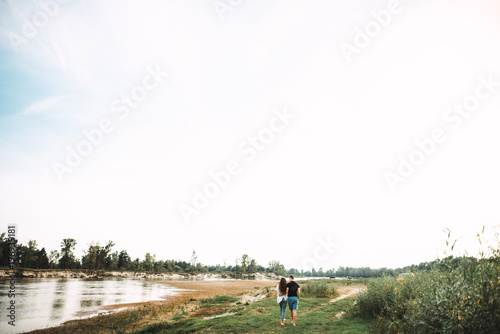 Happy young parents are walking in the countryside near the river with their little baby