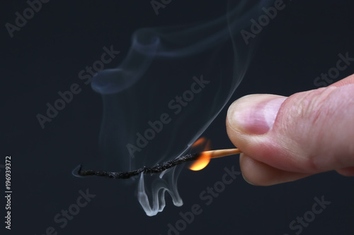 Burning and smoking wooden match in hand on dark background