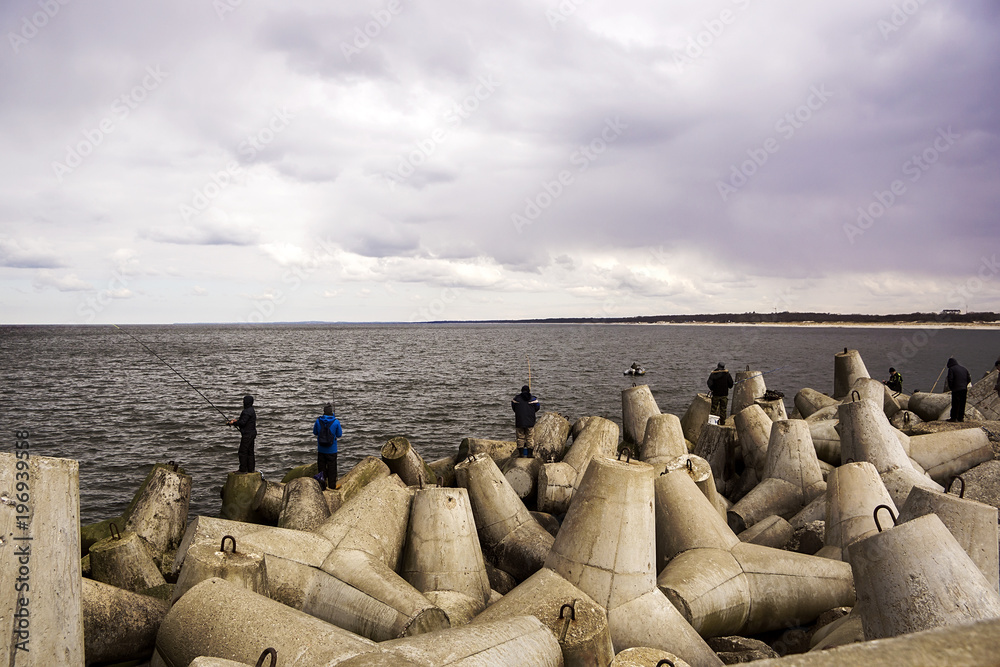 Many fishermen catch fish at the sea standing on big boulders.