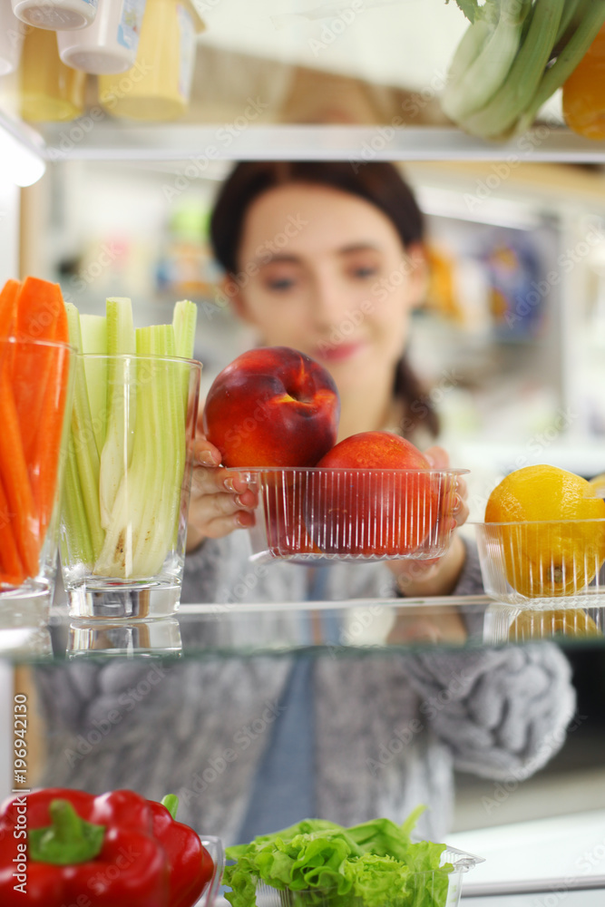 Portrait of female standing near open fridge full of healthy food, vegetables and fruits