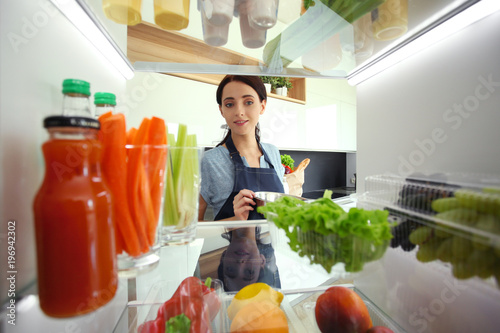 Portrait of female standing near open fridge full of healthy food  vegetables and fruits