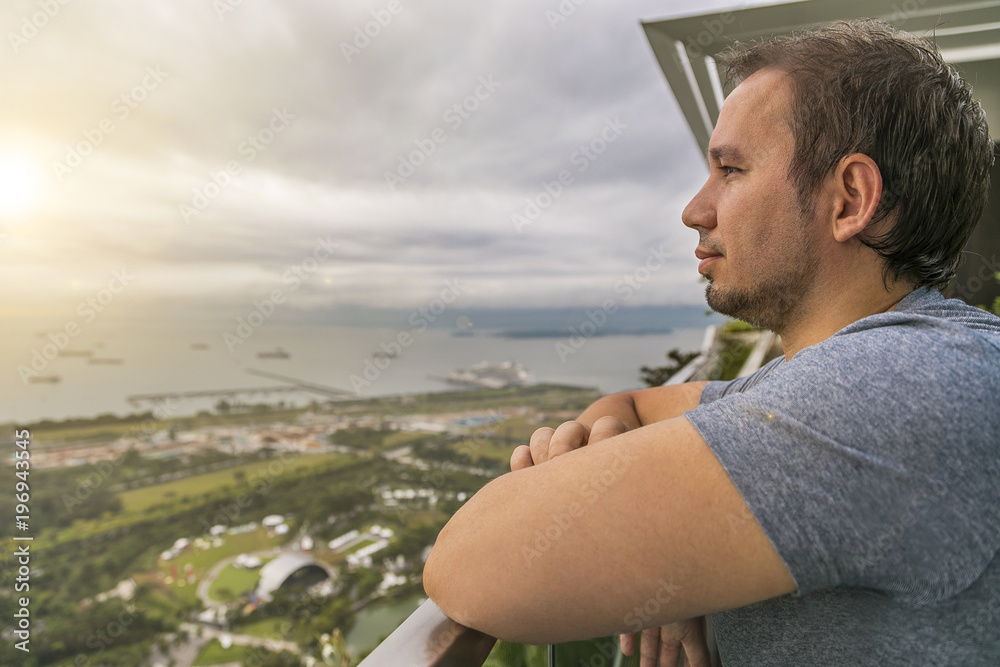 мужчина смотрит на залив с высоты небоскреба марина бэй сандс на фоне рассвета 
