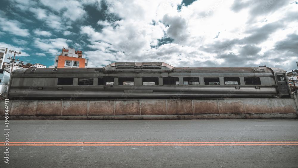 Fototapeta premium Wide-angle view of an abandoned retro railway carriage transformed into the buffet car lonely standing near the highway in foreground; forsaken grungy railroad dining-car with a road in front