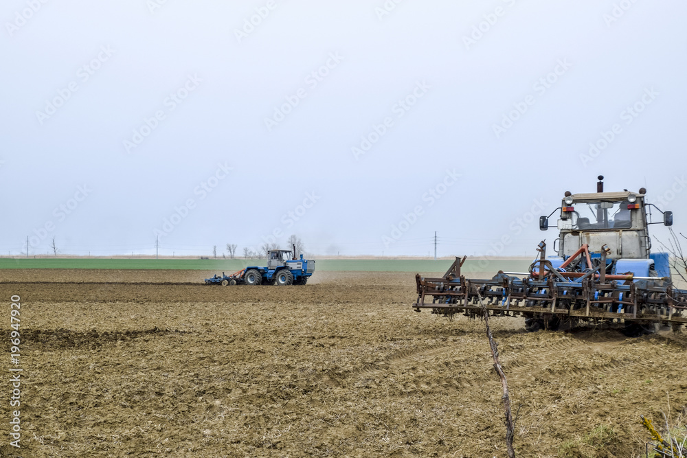 Fototapeta premium Lush and loosen the soil on the field before sowing. The tractor plows a field with a plow