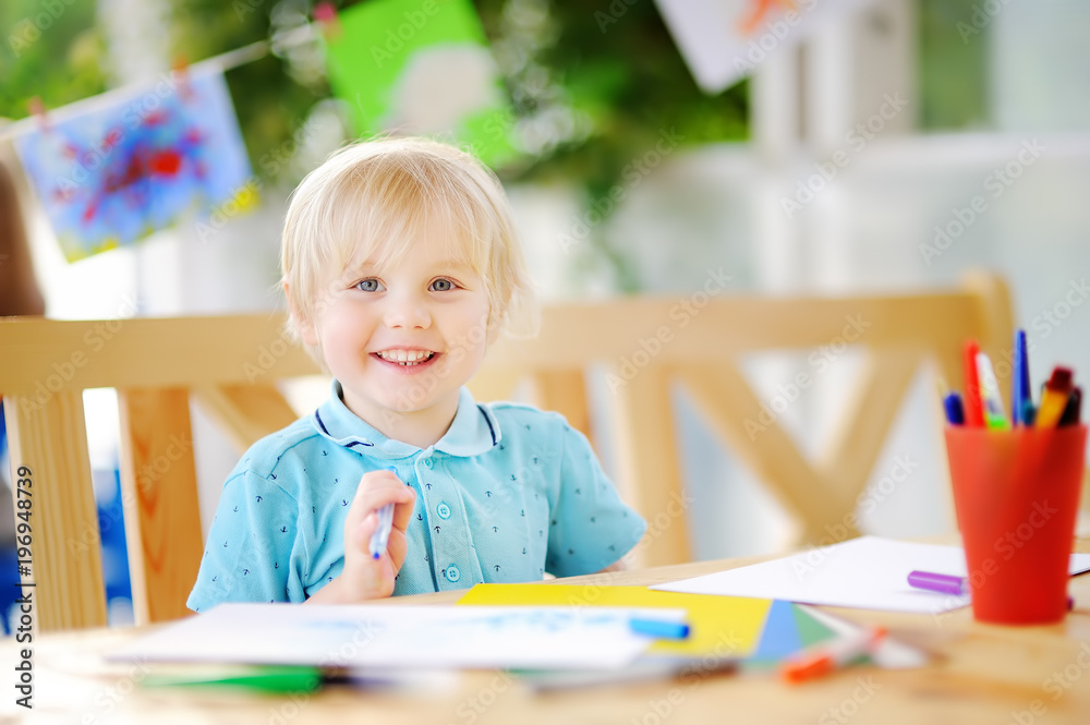 Cute little boy drawing and painting with colorful markers at kindergarten