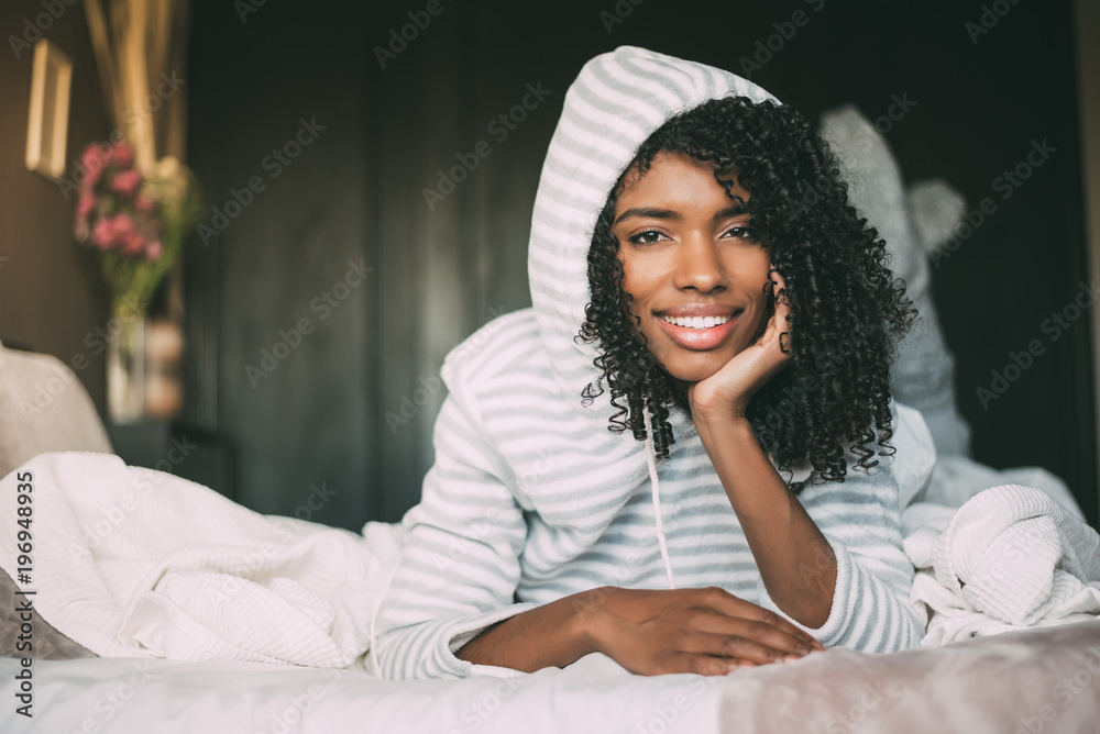 close up of a pretty black woman with curly hair smiling and lying on bed looking at the camera close up of a pretty black woman with curly hair smiling and lying on bed looking at the camera