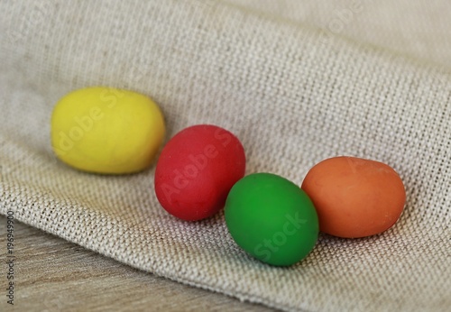 Four colorful - yellow, red, green and orange little eggs made of plasticine, easter theme placed on woven fabric, wooden table, pills