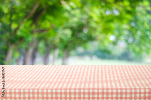 Empty table with pink and white tablecloth over blurred park nature background, for product display montage, spring and summer