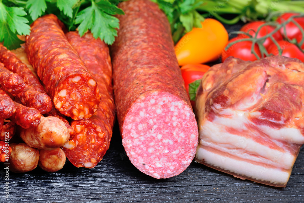 Sausages, salami and smoked bacon with vegetables on table Sausages, salami and smoked bacon with vegetables on table