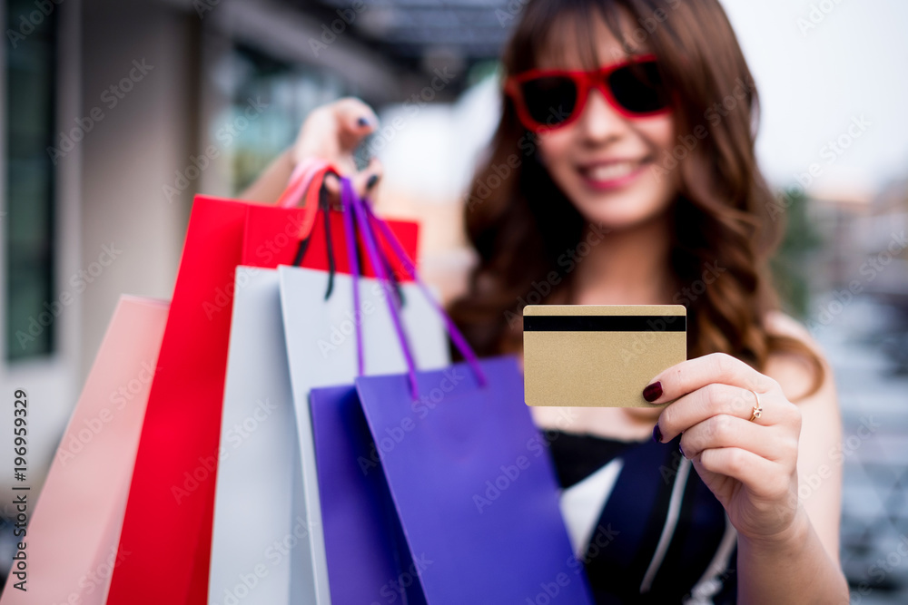 Happy woman wearing sunglasses posing with shopping bags and credit card, shopping concept Happy woman wearing sunglasses posing with shopping bags and credit card, shopping concept