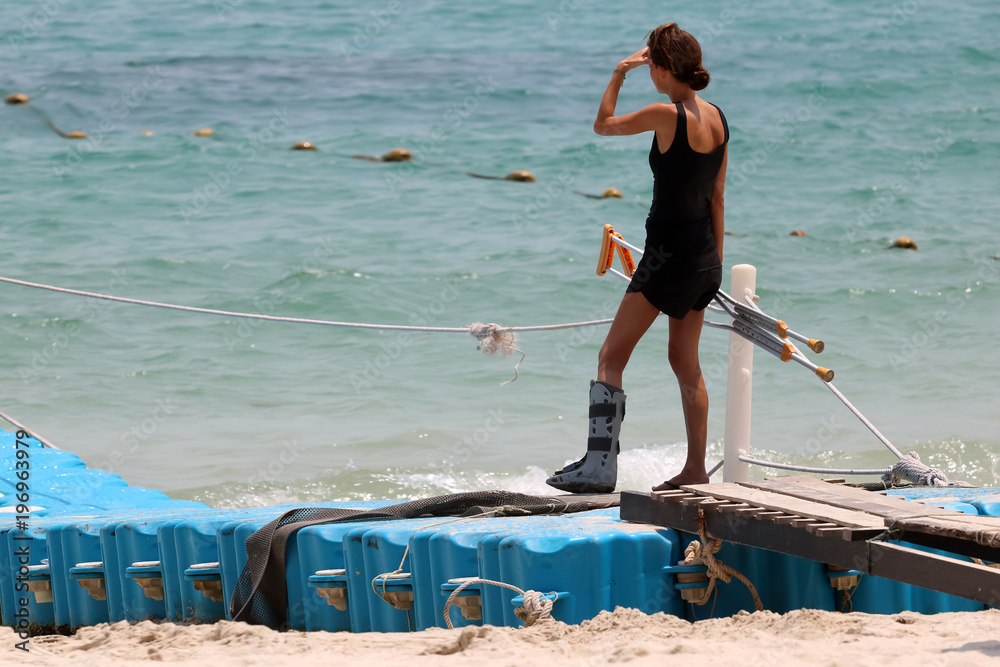 Φωτογραφία Accident tourist girl are walking up by crutches to the floating pier on the bea