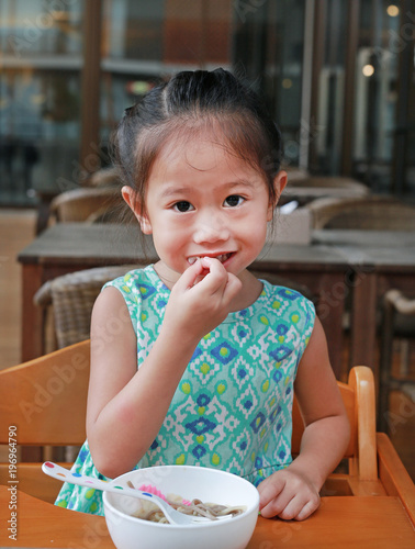 Smiling little asian girl at restaurant having breakfast with looking camera.