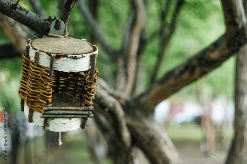 Unusual braided birdhouse on tree in urban environment.