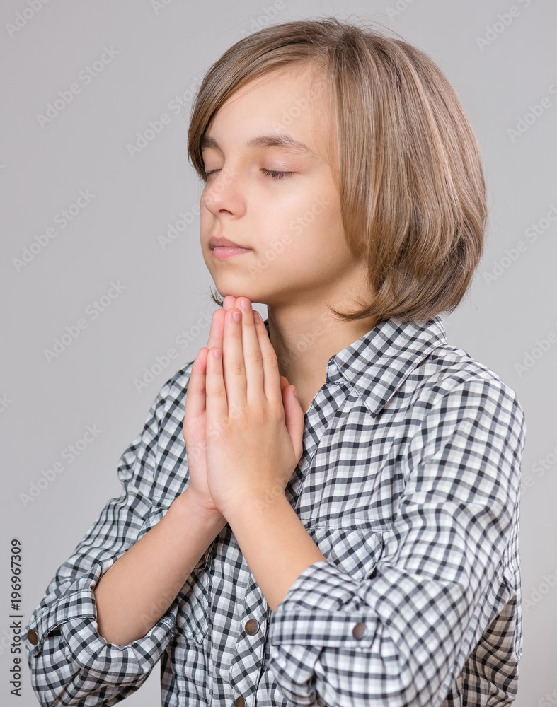 Portrait of beautiful caucasian teen girl on gray background. Schoolgirl showing different emotions - praying with folded hands, religion concept. Portrait of beautiful caucasian teen girl on gray background. Schoolgirl showing different emotions - praying with folded hands, religion concept.